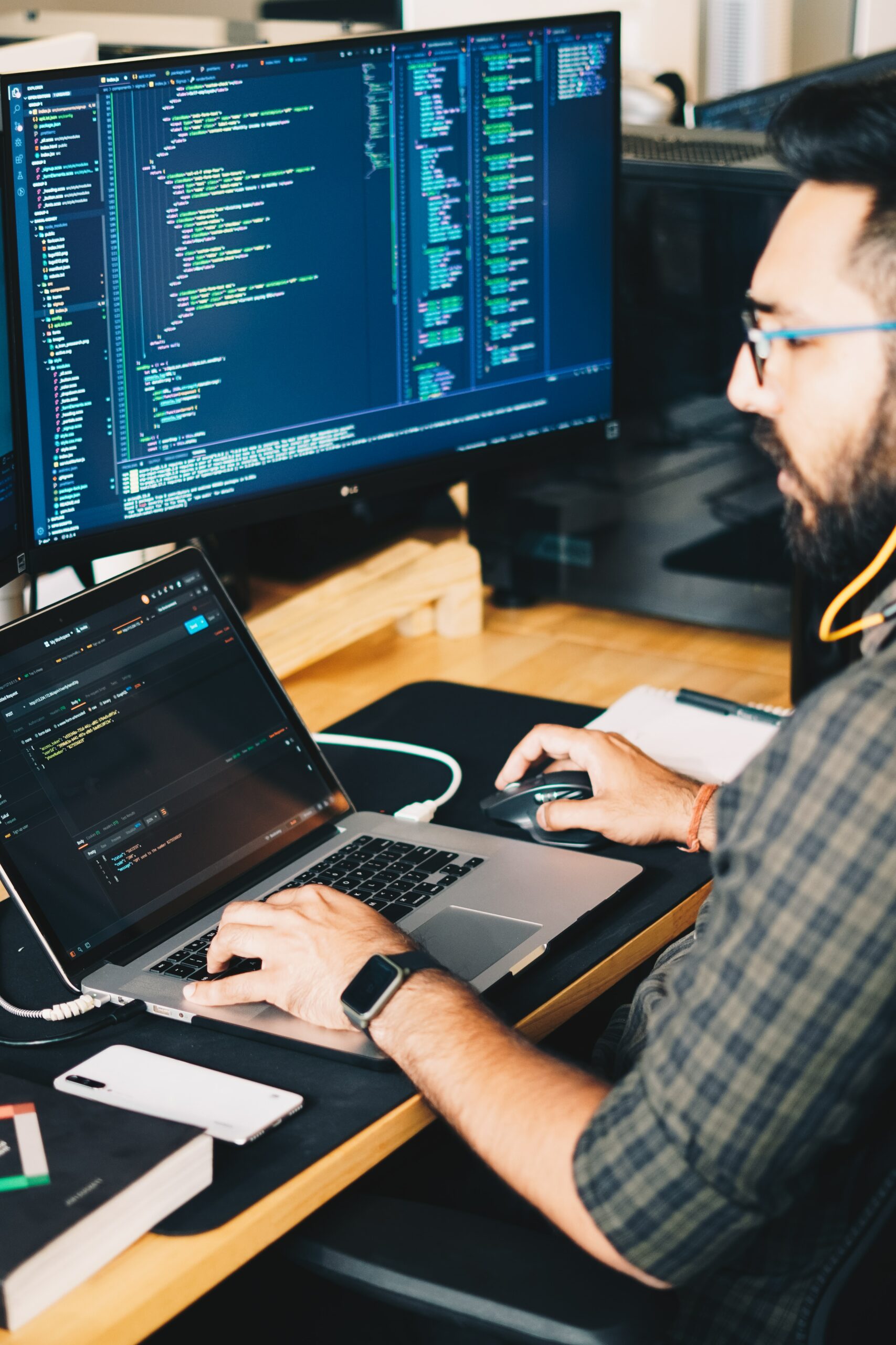 man is developing an app in between two computers. He has a clock on his arm.