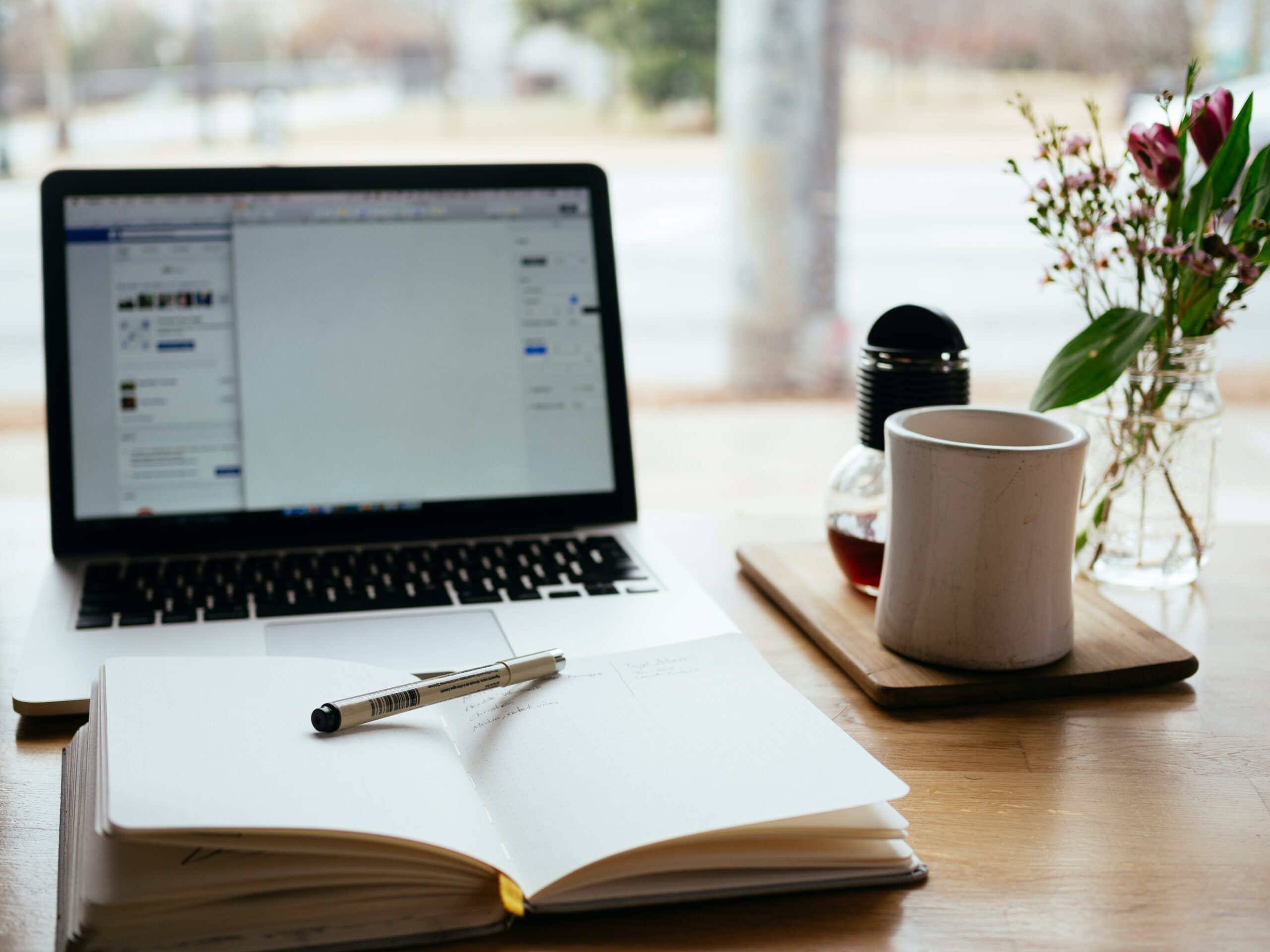a-laptop-is-standing-on-the-table-there-is-also-a-notebook-with-a-pen-and-a-cup-of-coffee
